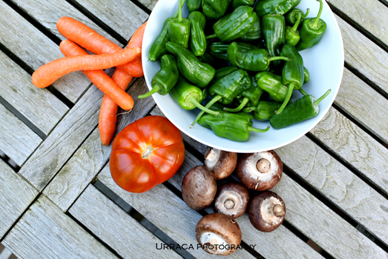 Small green peppers in white bowl carrots tomato and mushrooms o a wooden table